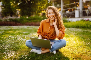 Genç bir kadın parkta oturmuş video görüşmesiyle iletişim kuruyor. Laptop bilgisayarına bakan bir kız, online konferans mesafesinde ofis sohbeti, sanal eğitim. Serbest çalışma..