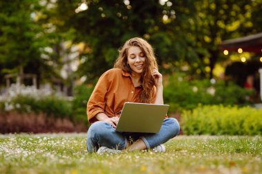 Genç bir kadın parkta oturmuş video görüşmesiyle iletişim kuruyor. Laptop bilgisayarına bakan bir kız, online konferans mesafesinde ofis sohbeti, sanal eğitim. Serbest çalışma..
