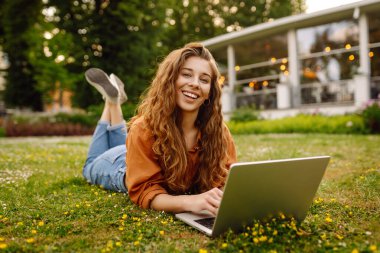 Genç bir kadın parkta oturmuş video görüşmesiyle iletişim kuruyor. Laptop bilgisayarına bakan bir kız, online konferans mesafesinde ofis sohbeti, sanal eğitim. Serbest çalışma..