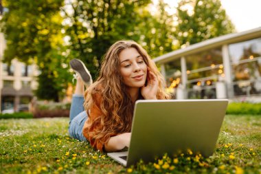 Genç bir kadın parkta oturmuş video görüşmesiyle iletişim kuruyor. Laptop bilgisayarına bakan bir kız, online konferans mesafesinde ofis sohbeti, sanal eğitim. Serbest çalışma..