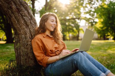 Genç bir kadın parkta oturmuş video görüşmesiyle iletişim kuruyor. Laptop bilgisayarına bakan bir kız, online konferans mesafesinde ofis sohbeti, sanal eğitim. Serbest çalışma..