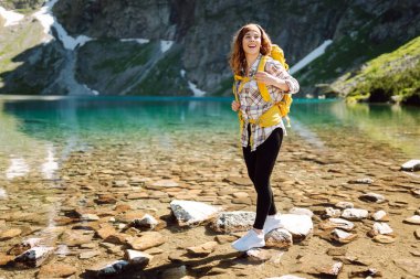 Sırt çantalı genç gezgin kız bir dağ gölünün kıyısına yürüyor. Dağlarda yürüyüş. Etkin yaşam biçimi.