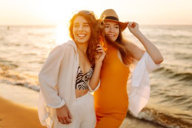 Yaz gününde gün batımında sahilde dinlenen iki güzel kadının portresi. Seyahat, hafta sonu, rahatlama ve yaşam tarzı konsepti.