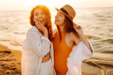 Yaz gününde gün batımında sahilde dinlenen iki güzel kadının portresi. Seyahat, hafta sonu, rahatlama ve yaşam tarzı konsepti.