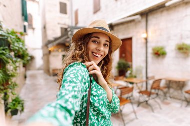 Güzel bir kadın sokakta yürüyor ve akıllı telefon kamerasıyla selfie çekiyor. Blogculuk, teknoloji, yaşam tarzı, seyahat, turizm, aktif yaşam.
