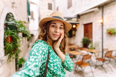 Güzel bir kadın sokakta yürüyor ve akıllı telefon kamerasıyla selfie çekiyor. Blogculuk, teknoloji, yaşam tarzı, seyahat, turizm, aktif yaşam.