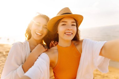 Neşeli kadınlar sahilde eğlenirken selfie çekiyorlar. Arkadaşlar birlikte. Seyahat, blog, hafta sonu, rahatlama ve yaşam tarzı konsepti.