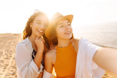 Neşeli kadınlar sahilde eğlenirken selfie çekiyorlar. Arkadaşlar birlikte. Seyahat, blog, hafta sonu, rahatlama ve yaşam tarzı konsepti.