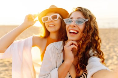 Neşeli kadınlar sahilde eğlenirken selfie çekiyorlar. Arkadaşlar birlikte. Seyahat, blog, hafta sonu, rahatlama ve yaşam tarzı konsepti.