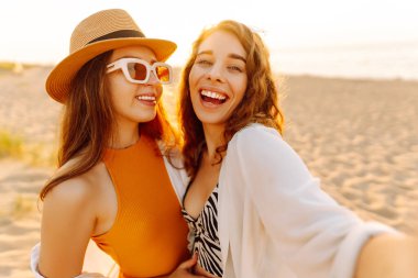 Neşeli kadınlar sahilde eğlenirken selfie çekiyorlar. Arkadaşlar birlikte. Seyahat, blog, hafta sonu, rahatlama ve yaşam tarzı konsepti.
