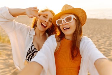 Neşeli kadınlar sahilde eğlenirken selfie çekiyorlar. Arkadaşlar birlikte. Seyahat, blog, hafta sonu, rahatlama ve yaşam tarzı konsepti.
