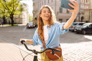 Çekici bir kadın eski Avrupa şehrinin caddesinde bisikletiyle selfie çekiyor. Arkadaşların ve ailenle uzaktan iletişim kurmak. Selfie zamanı..