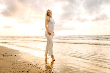 Mutlu kadın gün batımında sahilde yürüyor. Seyahat, hafta sonu, rahatlama ve yaşam tarzı konsepti.