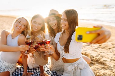 Bir grup mutlu bayan sahilde eğleniyor ve şarap içiyor, sahildeki bekarlığa veda partisinde selfie çekiyorlar. Seyahat, blog, hafta sonu, rahatlama ve yaşam tarzı konsepti.