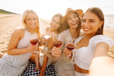 Bir grup mutlu bayan sahilde eğleniyor ve şarap içiyor, sahildeki bekarlığa veda partisinde selfie çekiyorlar. Seyahat, blog, hafta sonu, rahatlama ve yaşam tarzı konsepti.