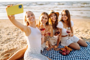 Bir grup mutlu bayan sahilde eğleniyor ve şarap içiyor, sahildeki bekarlığa veda partisinde selfie çekiyorlar. Seyahat, blog, hafta sonu, rahatlama ve yaşam tarzı konsepti.