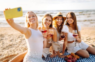 Bir grup mutlu bayan sahilde eğleniyor ve şarap içiyor, sahildeki bekarlığa veda partisinde selfie çekiyorlar. Seyahat, blog, hafta sonu, rahatlama ve yaşam tarzı konsepti.
