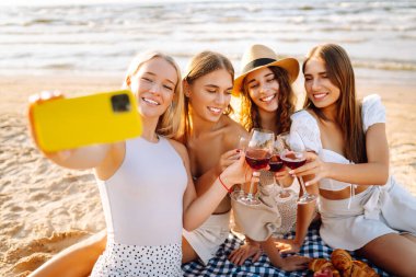 Bir grup mutlu bayan sahilde eğleniyor ve şarap içiyor, sahildeki bekarlığa veda partisinde selfie çekiyorlar. Seyahat, blog, hafta sonu, rahatlama ve yaşam tarzı konsepti.