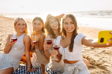 Bir grup mutlu bayan sahilde eğleniyor ve şarap içiyor, sahildeki bekarlığa veda partisinde selfie çekiyorlar. Seyahat, blog, hafta sonu, rahatlama ve yaşam tarzı konsepti.