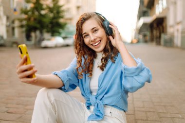 Sokakta yürüyen, müzik dinleyen ve selfie çeken mutlu bir kadın. Kasaba yaşam tarzları. Seyahat, turizm, teknoloji, blog konsepti.