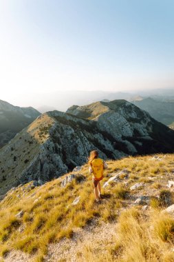 Dağ yamacında gezgin kadın gezgin. Manzaranın tadını çıkarıyor. Sırt çantasıyla dağlarda yürüyüş. Macera aktif.