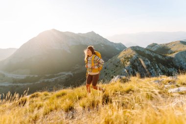 Dağ yamacında gezgin kadın gezgin. Manzaranın tadını çıkarıyor. Sırt çantasıyla dağlarda yürüyüş. Macera aktif.