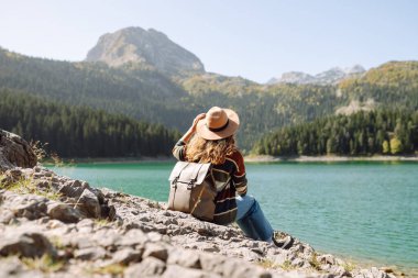 Genç bir kadın gezgin temiz havanın ve güzel bir göl ve dağ manzarasının tadını çıkarıyor. Aktif yaşam tarzı. Doğa, turizm konsepti.