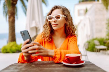 Kahve dükkanında cep telefonu olan güzel bir genç kadının portresi. İnsanlar, moda, yaşam tarzı, seyahat ve blog konsepti.