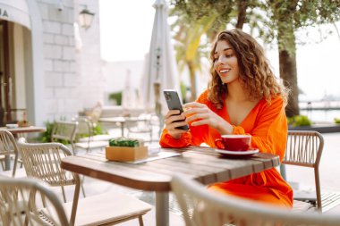 Kahve dükkanında cep telefonu olan güzel bir genç kadının portresi. İnsanlar, moda, yaşam tarzı, seyahat ve blog konsepti.