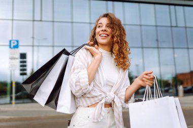 Alışveriş yaptıktan sonra şehirde dolaşan alışveriş çantalı bir kadın. Tüketim, satış, alım, alışveriş, yaşam tarzı konsepti.