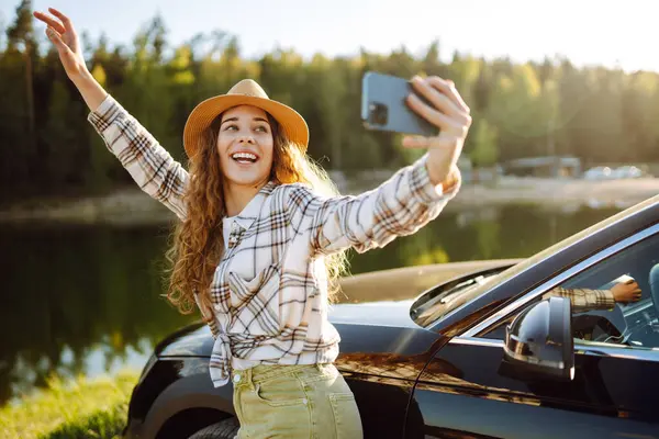 stock image Young female tourist traveling by car taking selfie. Rest stop in car trip to take photos. Active lifestyle, blogging, nature, weekend.