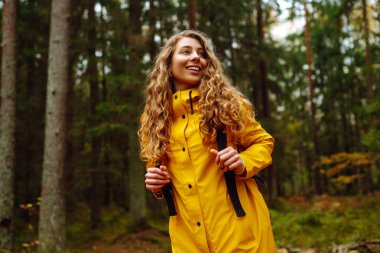 Ormanda uzun çam ağaçlarının arasında yürüyüş yapan bir kadın etrafa bakıyor. Seyahatler. Etkin yaşam biçimi.