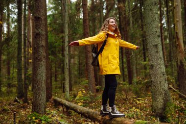 Ormanda uzun çam ağaçlarının arasında yürüyüş yapan bir kadın etrafa bakıyor. Seyahatler. Etkin yaşam biçimi.