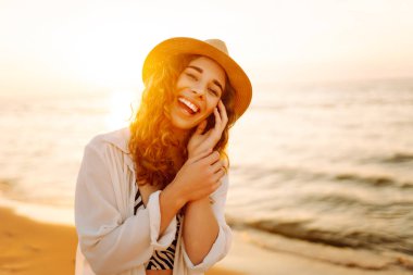 Gün batımında sahilde yürüyen mutlu bir kadın. Gün batımında deniz manzarası ve güzel bir gökyüzü. Seyahat, hafta sonu, rahatlama ve yaşam tarzı konsepti.