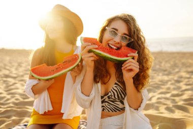Kumsalda karpuzlu gülen iki kadın. Piknik. İnsanlar, yaşam tarzı, seyahat, doğa ve tatil kavramı.