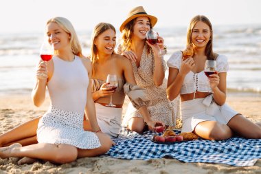 Bir grup genç kadın gün batımında sahilde eğleniyor ve içki içiyor. Kumsalda kızlar partisi. Tatil, dinlenme, tatil, piknik.