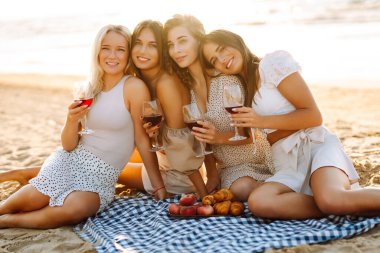 Bir grup genç kadın gün batımında sahilde eğleniyor ve içki içiyor. Kumsalda kızlar partisi. Tatil, dinlenme, tatil, piknik.