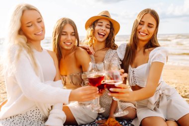 Bir grup genç kadın gün batımında sahilde eğleniyor ve içki içiyor. Kumsalda kızlar partisi. Tatil, dinlenme, tatil, piknik.