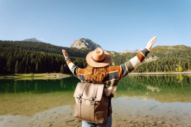 Sırt çantalı genç bayan güneşli bir havada dağ gölü manzarasına bakıyor. Seyahat, tatil kavramı..