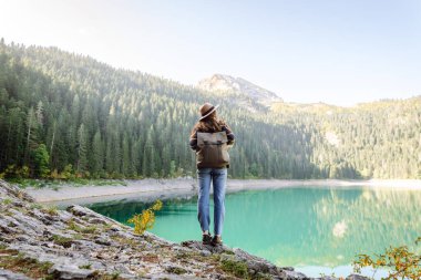 Sırt çantalı genç bayan güneşli bir havada dağ gölü manzarasına bakıyor. Seyahat, tatil kavramı..