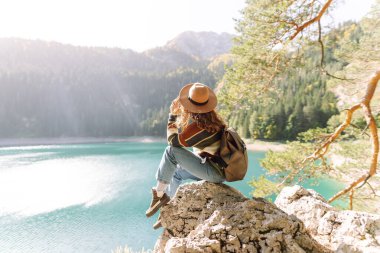 Sırt çantalı genç bayan güneşli bir havada dağ gölü manzarasına bakıyor. Seyahat, tatil kavramı..