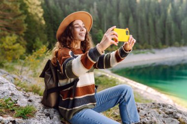 Genç gezgin dinleniyor ve tatildeyken dağlarla ve gölle muhteşem manzaranın fotoğraflarını çekiyor. Turizm, doğa, blog konsepti.