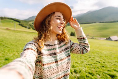 Dişi turist yeşil doğayla çevrili tepelerin ortasında selfie çekiyor. Teknoloji, seyahat, blog konsepti.