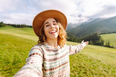Dişi turist yeşil doğayla çevrili tepelerin ortasında selfie çekiyor. Teknoloji, seyahat, blog konsepti.