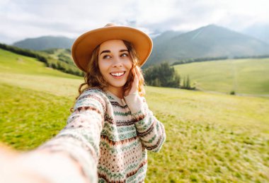 Dişi turist yeşil doğayla çevrili tepelerin ortasında selfie çekiyor. Teknoloji, seyahat, blog konsepti.