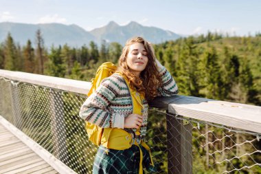 Sırt çantalı genç bir gezgin ağaç tepeleri arasında köprüden geçiyor. Özgürlük kavramı, seyahat, doğa.