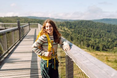 Sırt çantalı genç bir gezgin ağaç tepeleri arasında köprüden geçiyor. Özgürlük kavramı, seyahat, doğa.