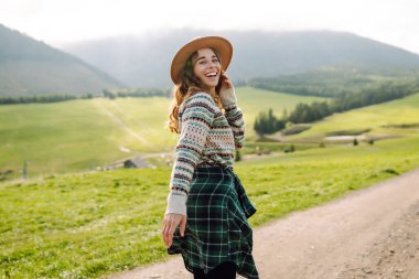 Yeşil çimen tarlasında yürüyen genç bir kadın, seyahat haftasonu manzarasına hayranlık duyan bir model. Boş hayaller kur.