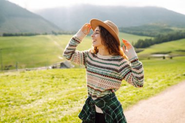 Yeşil çimen tarlasında yürüyen genç bir kadın, seyahat haftasonu manzarasına hayranlık duyan bir model. Boş hayaller kur.