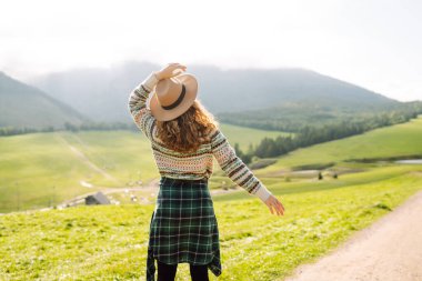 Yeşil çimen tarlasında yürüyen genç bir kadın, seyahat haftasonu manzarasına hayranlık duyan bir model. Boş hayaller kur.